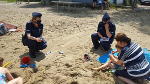 zdjęcie kolorowe: policjantki z katowickiej komendy rozmawiające o bezpiecznym wypoczynku nad wodą z plażowiczami nad stawem Morawa