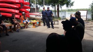 Na zdjęciu widać dwóch dzielnicowych oraz harcerzy siedzących na ławkach, z tyłu stoi podest z łódkami