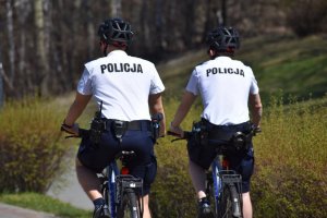 na zdjęciu widać policjantów w białych koszulkach siedzących na rowerach, na głowie mają założone kaski rowerowe
