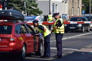 kolorowe zdjęcie: policjantka stoi wraz z funkcjonariuszem SOK przy samochodzie z tyłu widać przejazd kolejowo-drogowy.