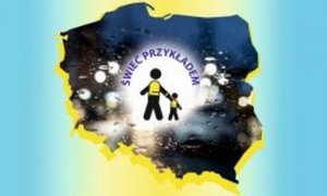 zdjęcie kolorowe: plakat promujący Ogólnopolski Policyjny Dzień Odblasków. Na żółto-niebieskim tle umieszczono kontur Polski w którym umieszczono postać osoby dorosłej i dziecka w kamizelkach odblaskowych oraz napis Świeć przykładem
