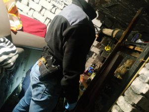 zdjęcie kolorowe: policjant operacyjny z katowickiej komendy ubrany w czarna bluzę podczas przeszukania pomieszczenia piwnicy