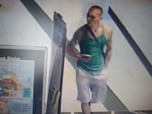 zdjęcie kolorowe: screen z zapisu monitoringu sklepowego przedstawiający mężczyznę w szarych krótki spodenkach, ciemnozielonym podkoszulku bez rękawów i czarnych okularach przeciwsłonecznych podejrzanego o kradzież perfum ze sklepu