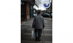 zdjęcie kolorowe: mężczyzna w podeszłym wieku idący chodnikiem i opierający się na lasce