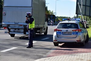 zdjęcie kolorowe: umundurowany policjant katowickiej drogówki z urządzeniem do pomiaru prędkości, wykonujący pomiar