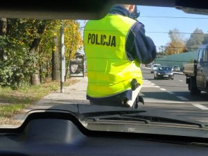zdjęcie kolorowe: policjant drogówki wykonujący kontrolę prędkości urządzeniem do wykonywania pomiaru