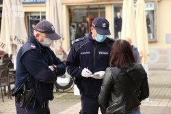 zdjęcie kolorowe: dwóch umundurowanych policjantów z maseczkami ochronnymi na twarzy rozmawiający z kobietą