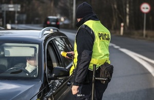 zdjęcie kolorowe: umundurowany policjant w kamizelce odblaskowej kontrolujący stan trzeźwości kierującego pojazdem osobowym