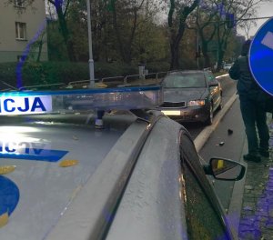 zdjęcie kolorowe: policyjny radiowóz, audi z uszkodzona szyba i techniki kryminalistyki wykonujący zdjęcia z miejsca zdarzenia