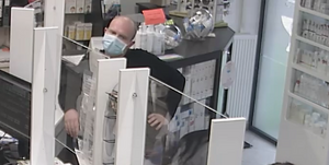 zdjęcie kolorowe: łysy wysoki mężczyzna ubrany w czarny sweter i niebieską  maseczkę ochronna na twarzy opierający się o kontuar w aptece