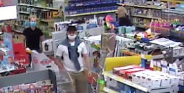 zdjęcie kolorowe: zapis z monitoringu sklepowego przedstawiających dwóch mężczyzn podejrzewanych o kradzież alkoholu, pierwszy z nich ubrany w beżowe długie spodnie, biała koszulkę z krótkim rękawem i przewieszonym przez ramiona szarym swetrem zawiązanym za rękawki na supeł opadający na klatkę piersiową mężczyzny, czarną czapeczkę z daszkiem i białą maseczkę ochronną założoną na usta. Drugi z mężczyzn ubrany w niebieskie długie jeansy, czarna koszulkę typu polo z krótkim rękawem, niebieską maseczkę ochronną założoną na usta i okulary przeciwsłoneczne czarne z błyszczącymi pomarańczowymi szybkami, które założone są na głowie