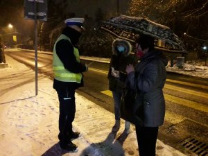 zdjęcie kolorowe: policjant wydziału ruchu drogowego katowickiej komendy rozmawiający w rejonie przejścia dla pieszych z dwoma kobietami