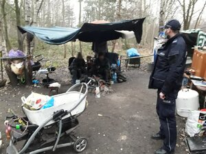 Zdjęcie kolorowe, na którym widać umundurowanego policjanta w miejscu przebywania osób bezdomnych na terenie leśnym.