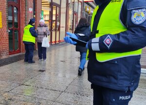 Zdjęcie kolorowe, na którym widać umundurowanego policjanta rozdającego odblaski na ulicy.