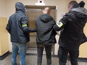zdjęcie kolorowe: dwóch nieumundurowanych policjantów z zatrzymanym przed drzwiami windy