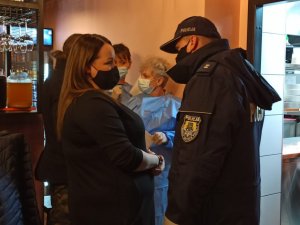 zdjęcie kolorowe: umundurowany policjant rozmawiający z kobietą w restauracji, w tle dwie przedstawicielki Państwowej Inspekcji sanitarnej