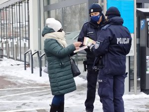 zdjęcie kolorowe: policjantka i policjant rozmawiający ze starszą kobietą o oszustwach w rejonie sklepu osiedlowego