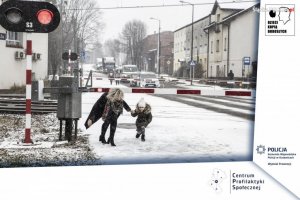 zdjęcie kolorowe: w zimowej scenerii kobieta z dziewczynką przechodząca przez przejazd kolejowy pomimo opuszczonych zapór