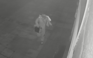 zdjęcie czarno-białe: niewyraźne zdjęcie mężczyzny idącego w nocy chodnikiem, który podejrzewany jest o kradzież torby