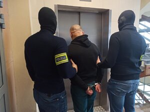 zdjęcie kolorowe: dwóch policjantów kryminalnych z zatrzymanym stojąc przed windą