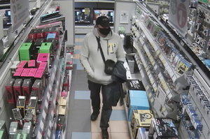 zdjęcie kolorowe: mężczyzna podejrzewany o kradzież w markecie ze sprzętem elektronicznym ubrany w ciemne buty sportowe, czarne spodnie, szara bluzę z dresu z kapturem i żółtą literą T na piersi, czarna czapeczkę z daszkiem i czarną maseczkę ochronna ma twarzy. Przez ramie przewieszona ma torebkę typu listonoszka