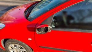 zdjęcie kolorowe: uszkodzony samochód osobowy koloru czerwonego z uszkodzonym lusterkiem bocznym