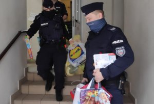 zdjęcie kolorowe: policjant i policjantka z Komisariatu IV Policji w Katowicach znoszą zapakowane torby z zabawkami po schodach