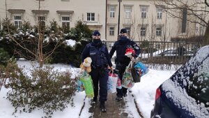 zdjęcie kolorowe: policjantka i policjant niosący prezenty do Domu Dziecka