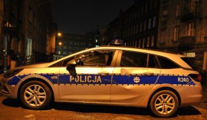 zdjęcie kolorowe: policyjny radiowóz zaparkowany przed komisariatem z uszkodzonymi szybami