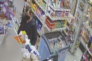 zdjęcie kolorowe: mężczyzna z krótko obciętymi włosami zaczesanymi na prawy bok, w granatowej kurtce i ciemnej maseczce ochronnej założonej na twarz stojący przy sklepowej ladzie