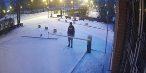 zdjęcie kolorowe: mężczyzna stojący przed zamkniętym szlabanem ubrany w szare spodnie dresowe i ciemna bluzę z kapturem z napisem Puma