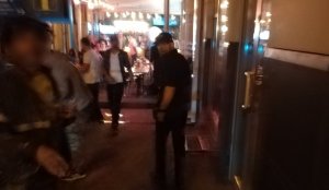 zdjęcie kolorowe: wieczór przed jedną z restauracji na ulicy Dyrekcyjnej w Katowicach, mężczyzna ubrany cza czarni z czarnym kaszkietem na głowie, zdjęcie zniekształcone ze względu na poruszenie obrazu
