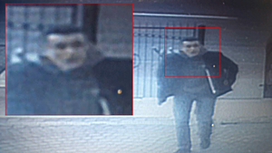 zdjęcie kolorowe: zdjęcie z zapisu monitoringu przedstawiające mężczyznę ubranego w ciemne ubrania na tle bramy