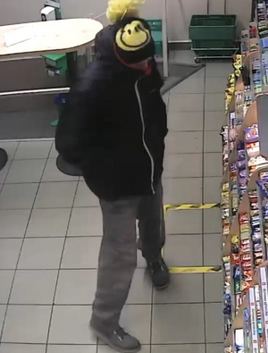 zdjęcie kolorowe: mężczyzna w czarnej czapce z żółtym pomponem, czarnej kurtce i szarych spodniach stojący przed sklepową lada