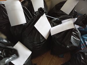 zdjęcie kolorowe: czarne plastikowe worki z załączonymi do nich białymi kartkami formatu A4, ustawione na podłodze