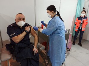 zdjęcie kolorowe: dzielnicowy przyjmujący pierwszą dawkę szczepienia oraz pielęgniarka i lekarz nadzorujący szczepienie