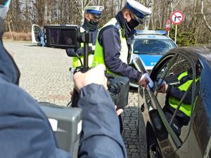 zdjęcie kolorowe: ręka operatora z telefonem i policjant przy samochodzie