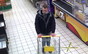 zdjęcie kolorowe: mężczyzna pchający sklepowy wózek, ubrany czarne buty, niebieskie spodnie, granatowa kurtkę z kapturem i szara bluzę dresową z kapturem z maseczka ochronną umieszczona pod brodą