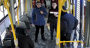 zdjęcie kolorowe: screen z monitoringu umieszczonego w tramwaju - dwóch młodych mężczyzna znajdujących się w tramwaju, pierwszy ubrany w czarne spodnie, niebieską długa kurtkę z czarnymi elementami po bokach kurtki i wełnianą czarno-białą czapką, drugi z mężczyzn ubrany w czarne spodnie, szare buty sportowe i czarną kurtkę z dwoma psami na piersi koloru czerwonego i białego