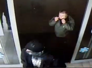 zdjęcie kolorowe: dwóch mężczyzn wchodzących do marketu, jeden ubrany w czarną kurtkę, czarną czapkę i maseczka ochronna na twarz, a drugi w zielona kurtkę i ciemne spodnie