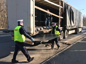 zdjęcie kolorowe: dwóch policjantów katowickiej drogówki niosących blachę do samochodu ciężarowe