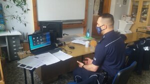 zdjęcie kolorowe: katowicki policjant siedzący w szkolnej ławce i prowadzący lekcje on-line