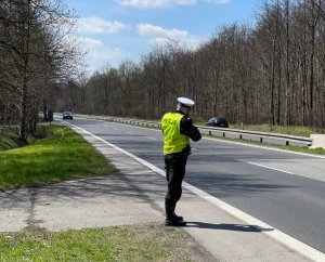 zdjęcie kolorowe: policjant katowickiej drogówki na skraju pasa jedni wykonujący pomiar prędkości pojazdu