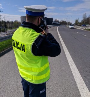 zdjęcie kolorowe: umundurowany policjant drogówki wykonujący pomiar prędkości pojazdu