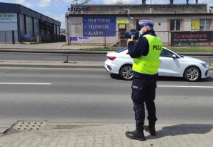 zdjęcie kolorowe: policjant drogówki dokonujący pomiaru prędkości samochodu osobowego
