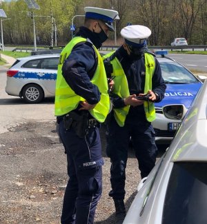 zdjęcie kolorowe: policjant wydziału prewencji i policjant ruchu drogowego na tle dwóch radiowozów wykonujący kontrolę drogową