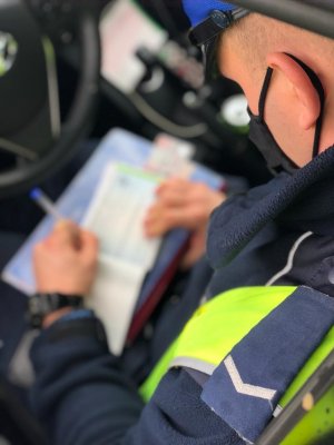 zdjęcie kolorowe: policjant drogówki sporządzający dokumentację z kontroli drogowej