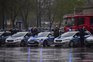 zdjęcie kolorowe: policyjne radiowozy, wóz straży pożarnej, policjanci i strażacy zebrani na placu przed katowickim Spodkiem