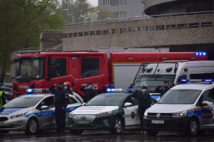 zdjęcie kolorowe: policyjne radiowozy i motocykle, a także wóz strażacki, policjanci i strażacy na placu przed spodkiem oddają honor zmarłemu policjantowi