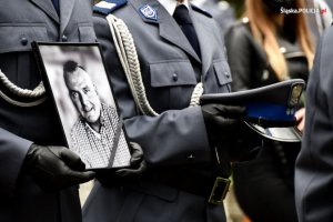 zdjęcie kolorowe: zdjęcie zmarłego asp. Michała Kędzierskiego trzymane w dłoniach przez policjanta